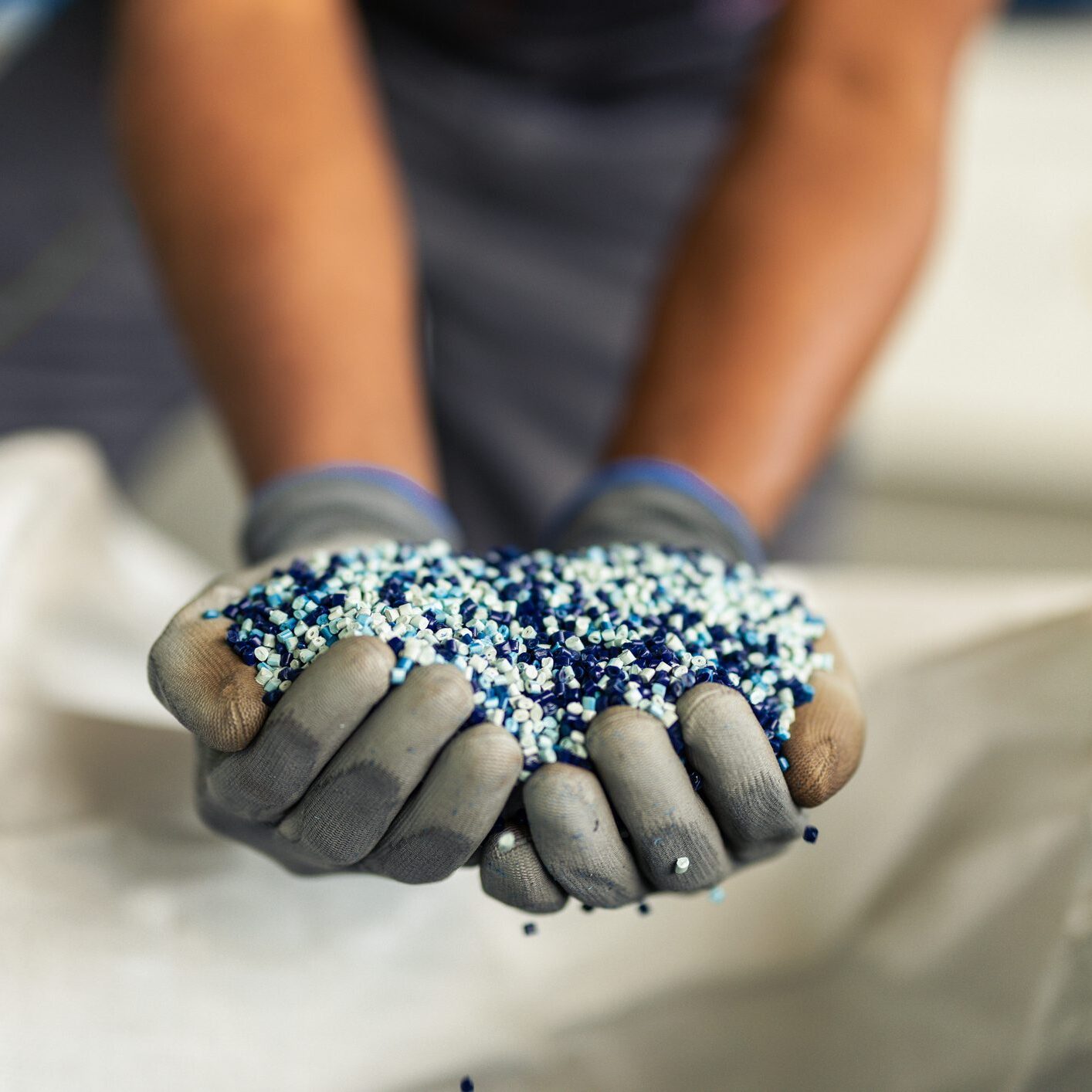 Unrecognizable worker at the recycling factory holding a bunch of plastic granules